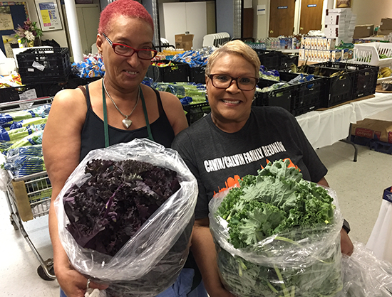 Two women holding bags of green and purple lettuce